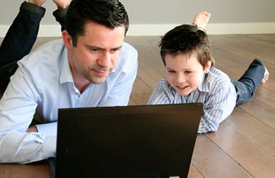 Vater und Sohn liegen auf dem Boden und schauen gemeinsam auf einen Laptop