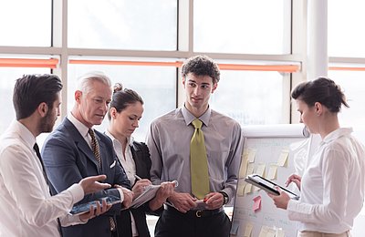 Fünf Geschäftsleute stehen zusammen und diskutieren Unterlagen in modernem Büro